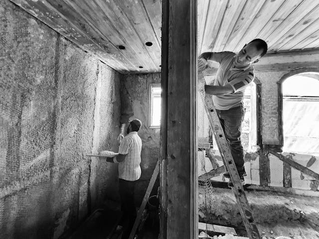 2 men working on plastering the walls.