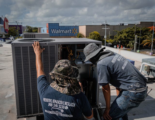 2 men checking the hvac system on a building.